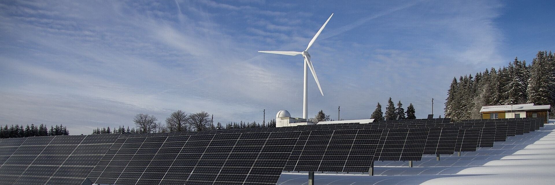 Im Vordergrund Solarpaneele, im Hintergrund ein Windrad inmitten einer Schneelandschaft