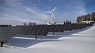 Im Vordergrund Solarpaneele, im Hintergrund ein Windrad inmitten einer Schneelandschaft